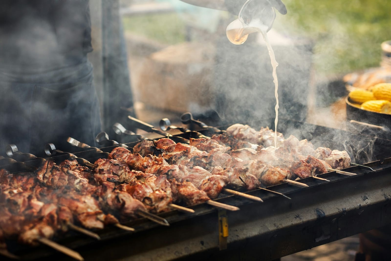 Pork skewers smoking over a charcoal grill as marinade is poured over them